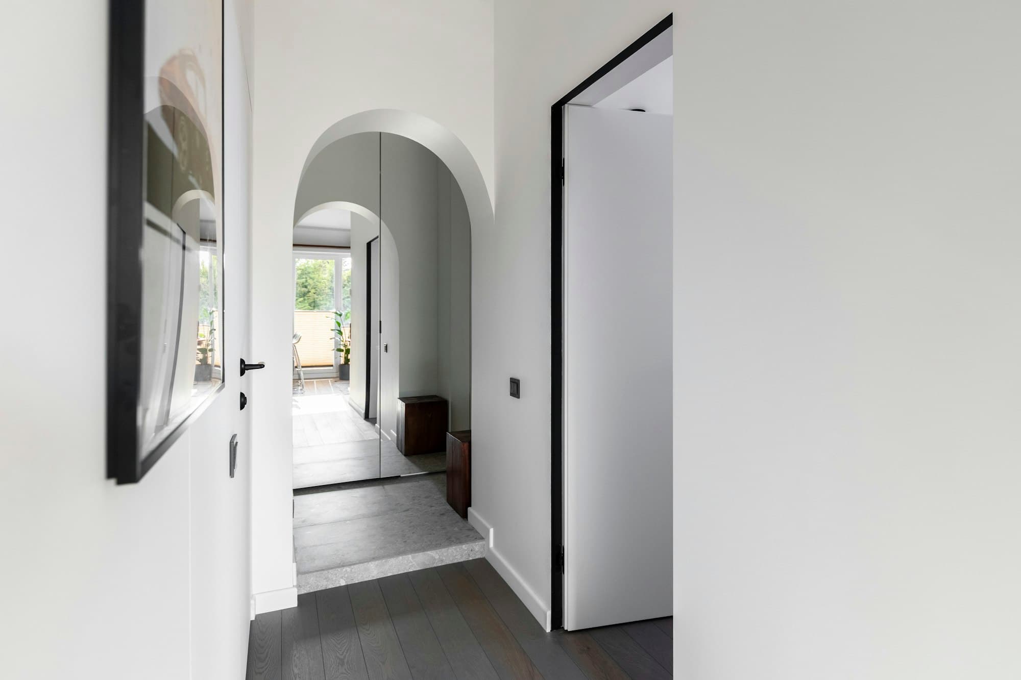 Couloir blanc avec passage en arche et porte noire toute hauteur